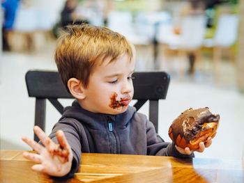 Cute toddler boy in casual clothes eating a chocolate bun in a food court there is a chocolate