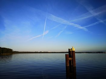Wooden posts in lake against blue sky