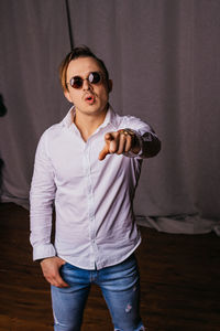 Portrait of young man wearing sunglasses standing against curtain