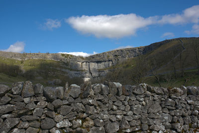 Stone wall by rocks against sky