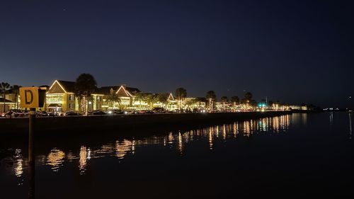 Illuminated buildings by lake against sky in city at night