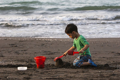 Full length side view of boy playing on sand at beach