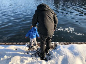 Rear view of father and son standing on snow covered pier by lake