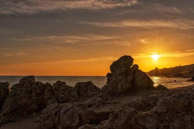 Rock formations on beach against sky during sunset