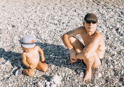 High angle view of shirtless grandfather with granddaughter sitting at beach