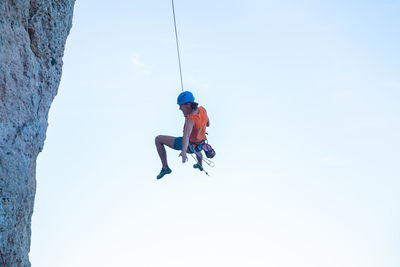 Low angle view of man swinging from rope against clear sky