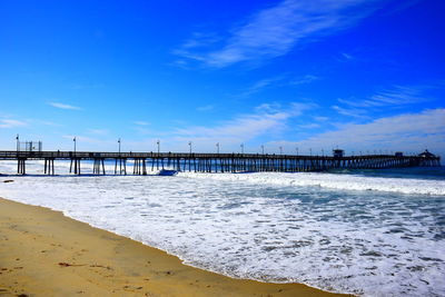 Pier on beach against blue sky