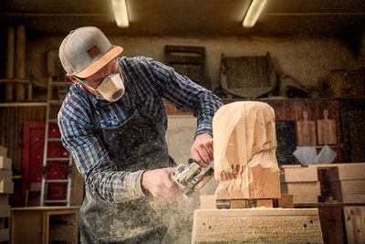 A young man carpenter in a suit, goggles saws a man's head with a tree 