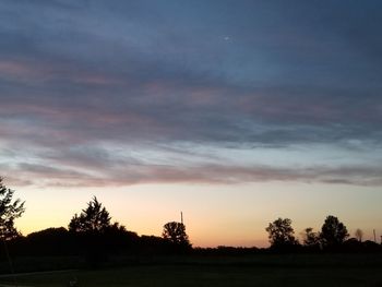 Silhouette trees on field against sky at sunset