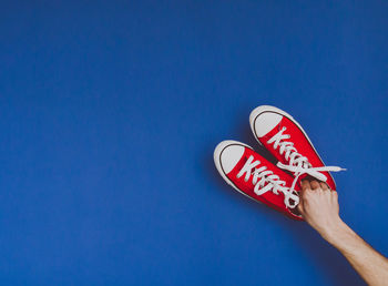 Cropped hand holding canvas shoes on blue background