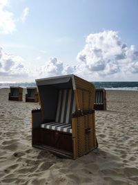 Hooded chairs on beach against sky