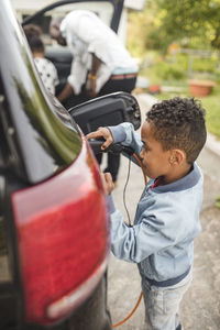 Side view of boy charging electric car while standing on driveway