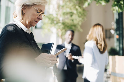 Senior businesswoman using mobile phone while entrepreneur are talking in background