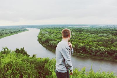 Side view of man standing against river by forest