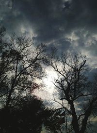 Low angle view of bare trees against cloudy sky