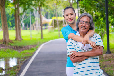 Portrait of smiling woman exercising with man against trees in park