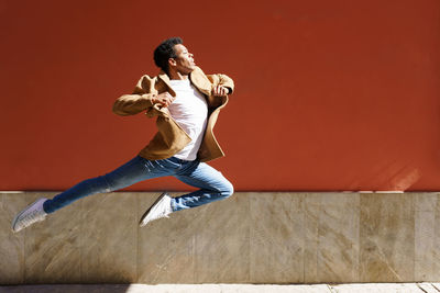 Full length of young woman jumping against wall