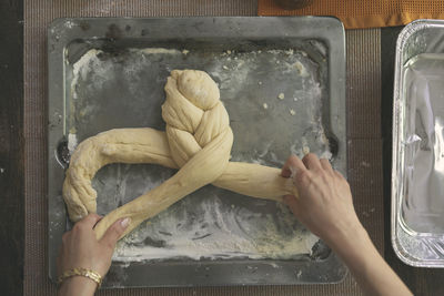 Cropped image of hands braiding dough for challah bread in tray at table