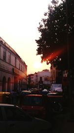 Cars on city street against sky during sunset