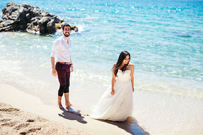 High angle view of newlywed couple walking at beach during sunny day