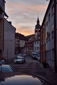 Cars on street by buildings against sky during sunset