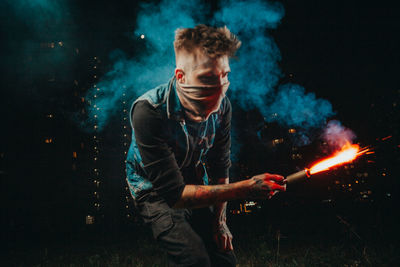 Young man holding burning fire at night