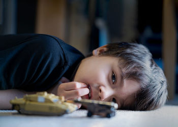 Portrait of upset boy lying on floor with toy