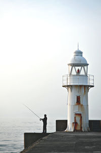 Low angle view of man fishing in sea against sky