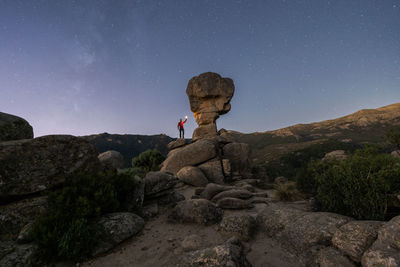 Low angle of anonymous explorer standing with illuminated flashlight near rock in highlands against night starry sky