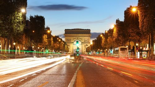 Light trails on city street by arc de triomphe against sky during dusk