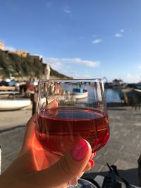 Close-up of hand holding beer glass against sky