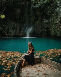 Woman sitting on rock by waterfall
