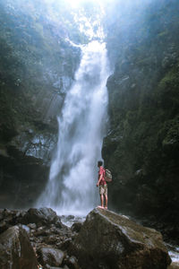 Side view of young man with backpack looking at waterfall while standing on rock