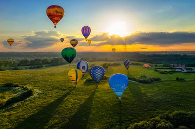 Hot air balloons flying over field against sky during sunset