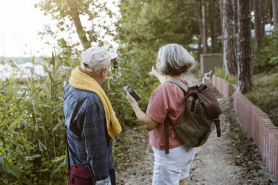 Senior couple with smart phone pointing while hiking in forest