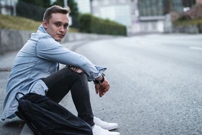 Side view portrait of young man sitting on road