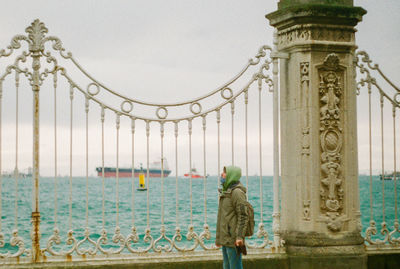 Rear view of man standing near old fence with a sea view