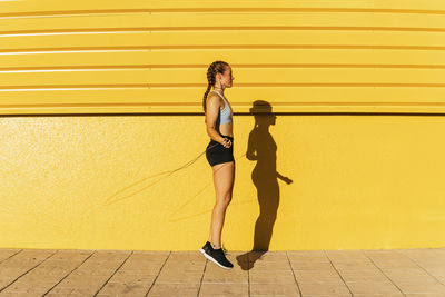 Full length of woman standing on footpath against yellow wall