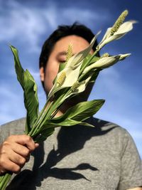Midsection of man holding peace lily flowers against the sky.