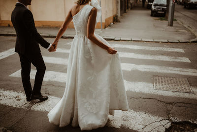 Low section of bride and bridegroom holding hands while crossing road