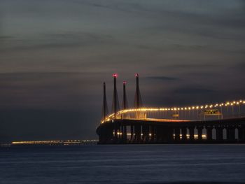 Illuminated bridge over sea against sky at night