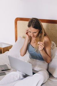 Caucasian woman adjusting headphones while working from her bed