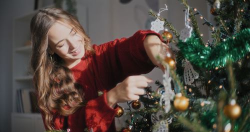 Portrait of young woman holding christmas tree at home
