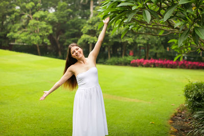 Full length of a smiling young woman standing on grass