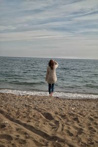 Rear view of woman standing on beach against sky