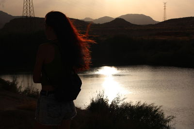 Rear view of woman standing on mountain against sunset sky