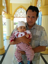 Portrait of father with baby standing at corridor