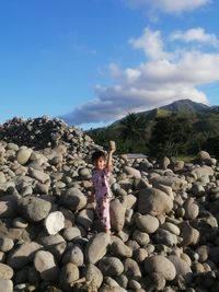 Rear view of a boy standing on rock against sky