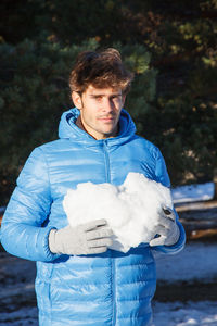 Portrait of young man holding snow standing outdoors