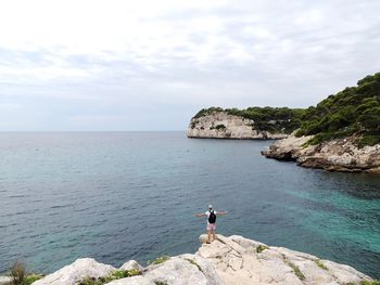 Rear view of man standing on rock formation in sea against sky